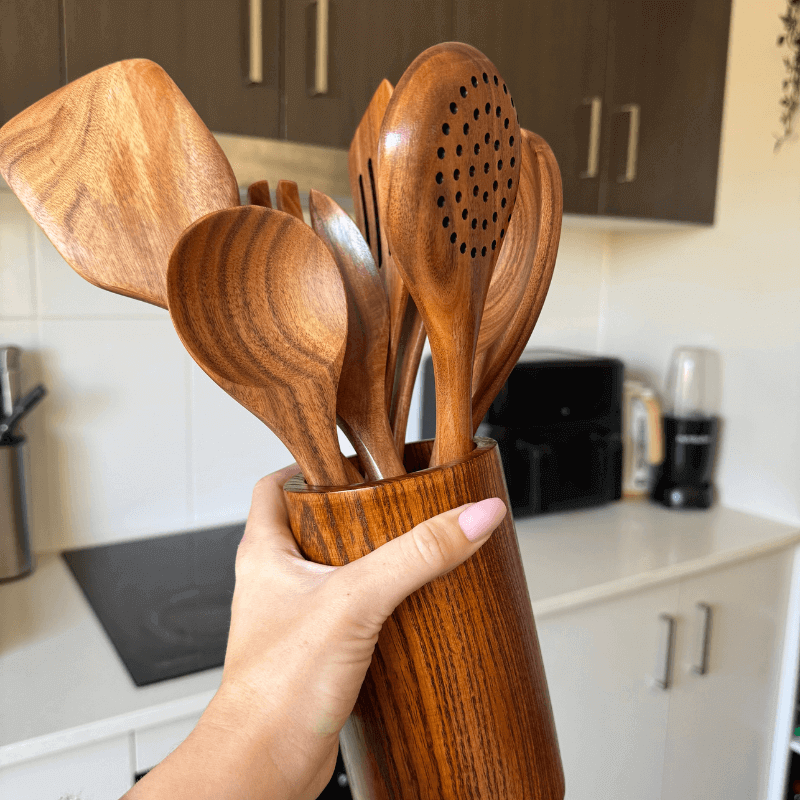 Hand holding a wooden utensil set in a kitchen