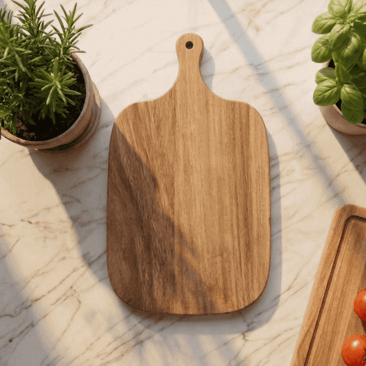 Wooden cutting board on a marble surface with plants and tomatoes.