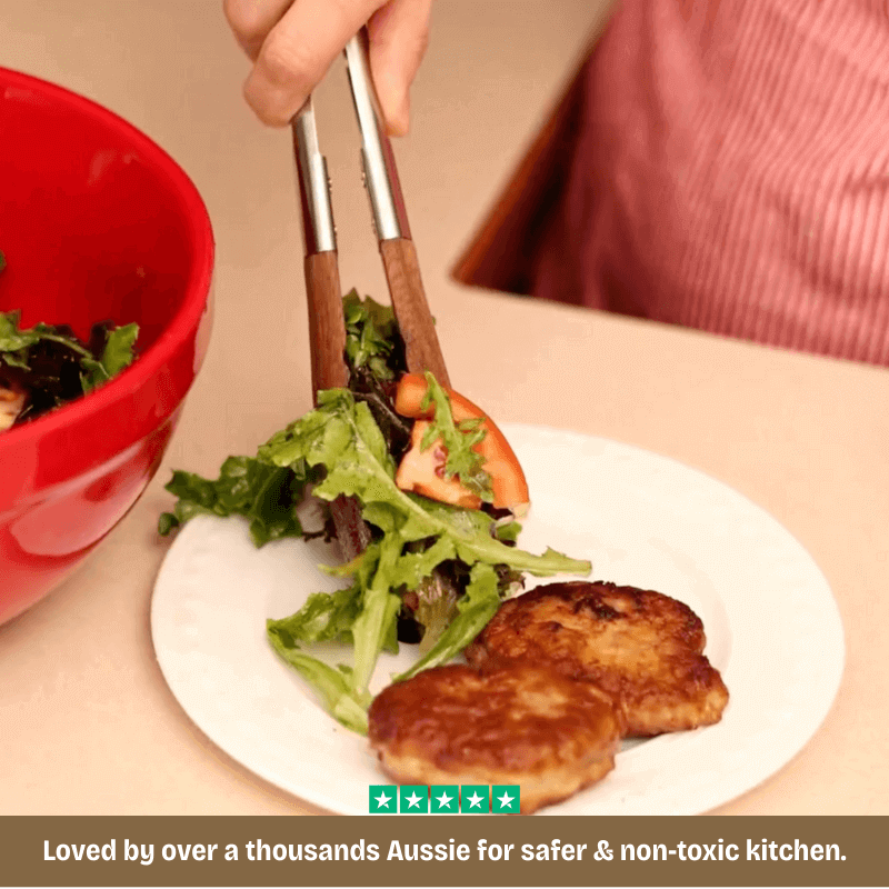 Person holding tongs over a plate of salad with a red bowl in the background