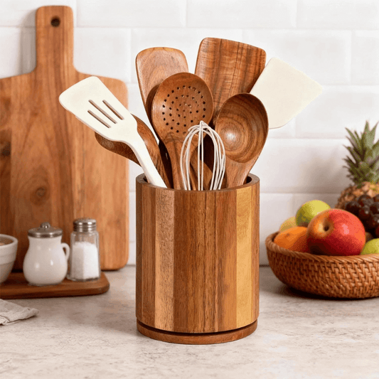 Wooden utensil holder with kitchen utensils on a countertop with fruits in the background