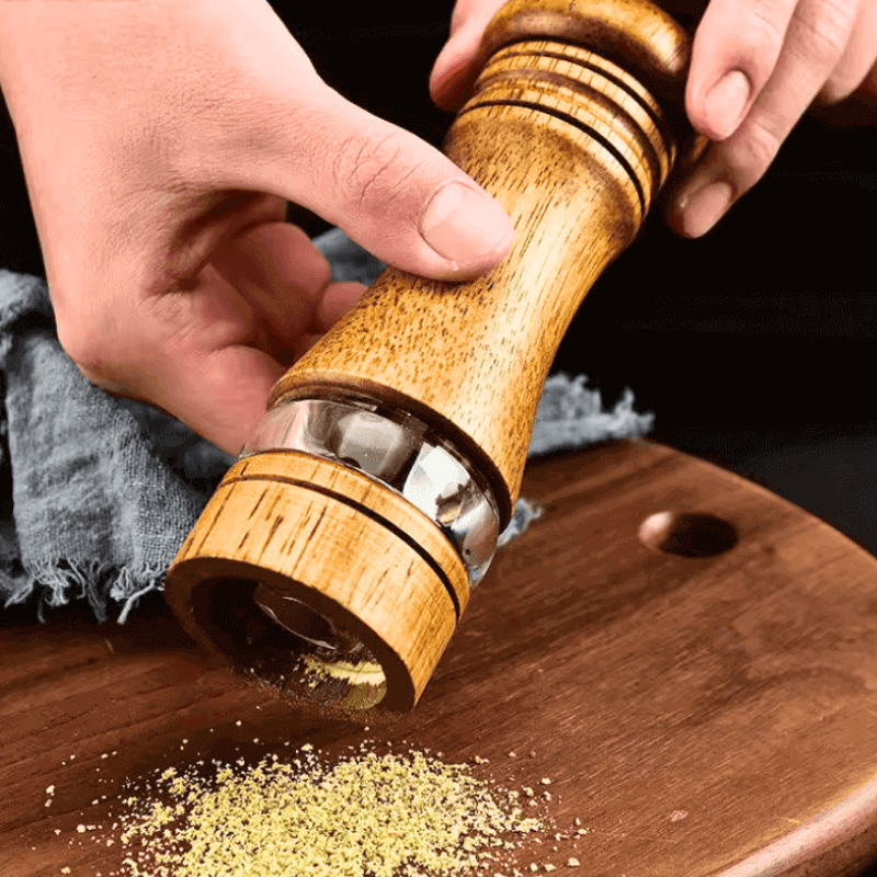 Wooden pepper grinder being used on a wooden surface with a dark background